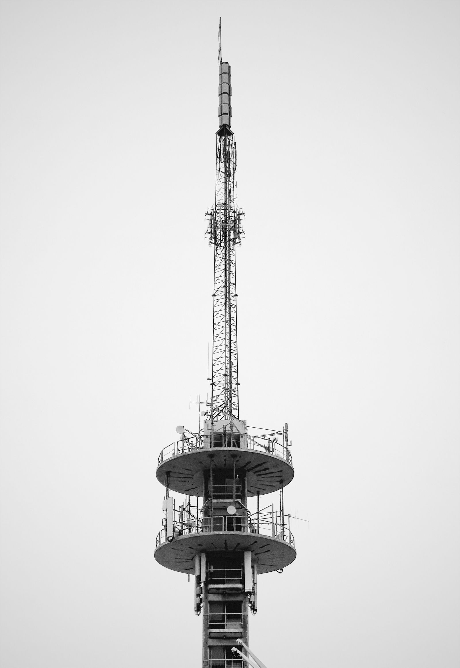 Torre de telecomunicações em preto e branco, com antenas e plataformas, contra um céu claro