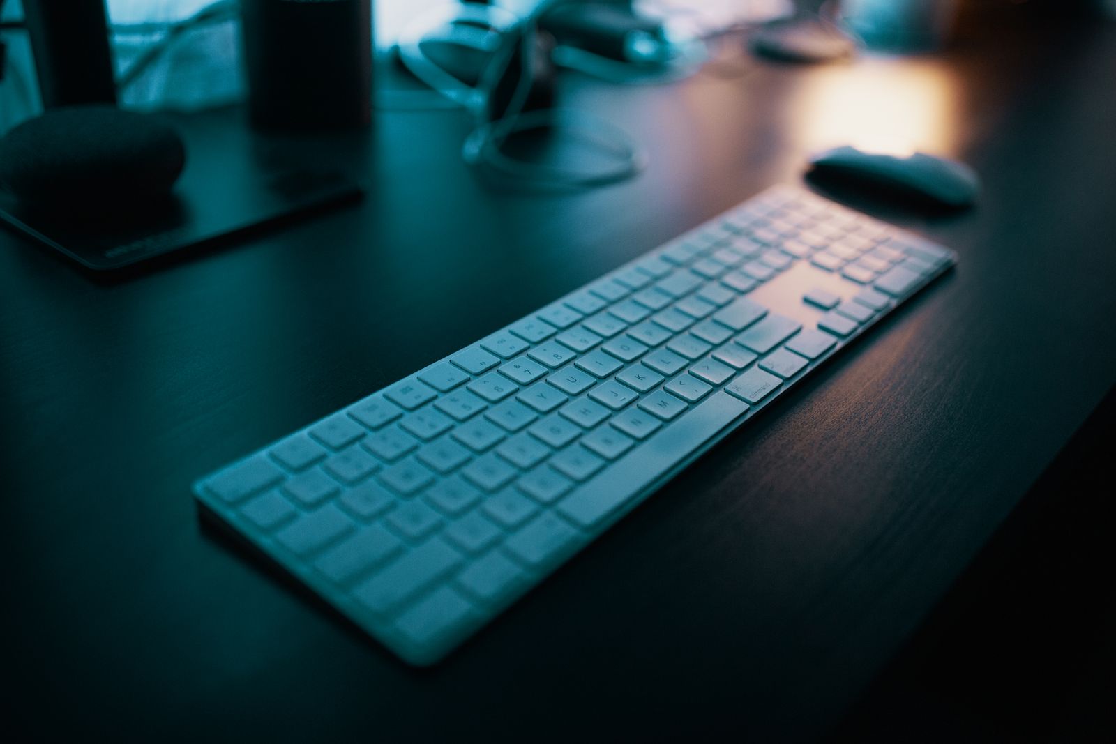 Teclado e mouse brancos sem fio sobre uma mesa escura sob luz azul fraca